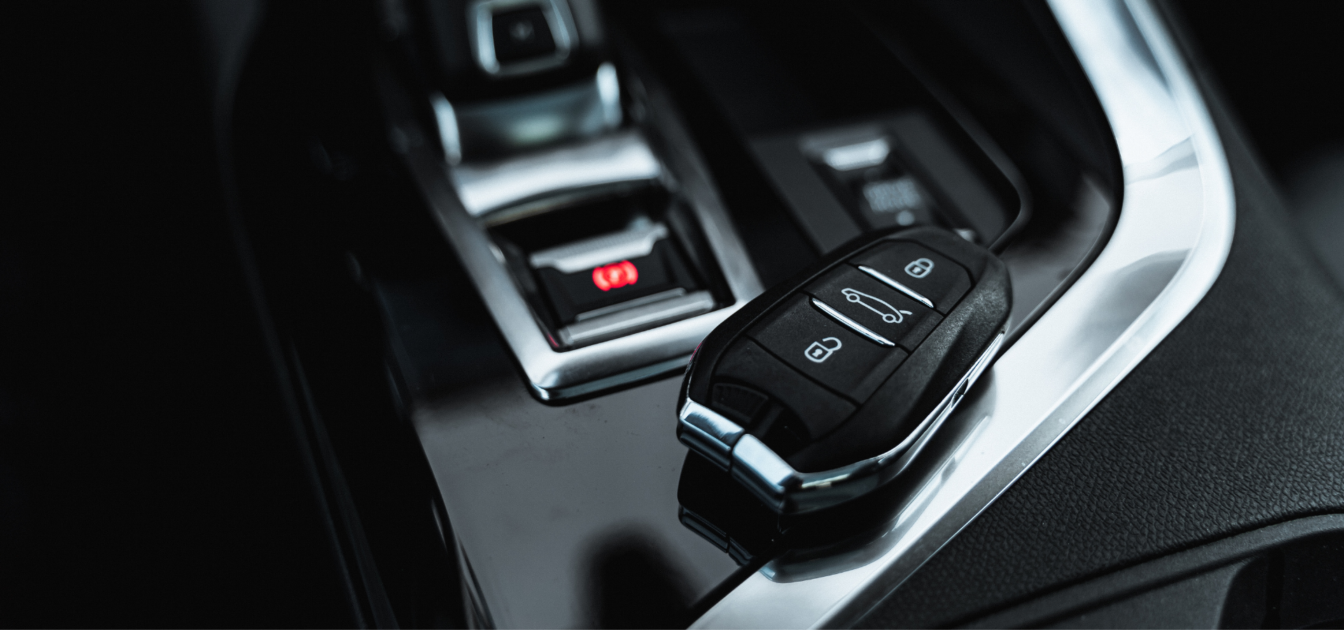 A modern car key fob resting on a vehicle's center console next to an electronic parking brake switch.
