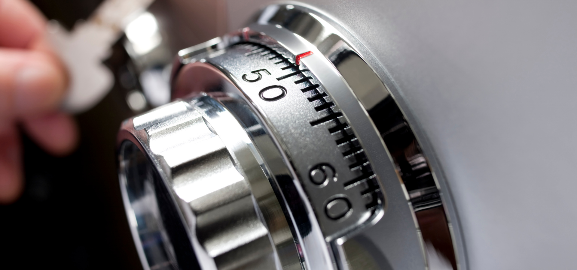 A hand holding a key near the chrome dial of a combination safe set between numbers 50 and 60.