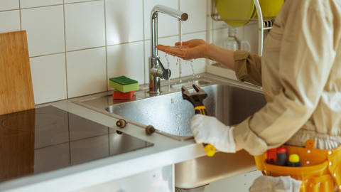 Person in workwear testing a kitchen faucet with a wrench. The faucet is running in the sink.