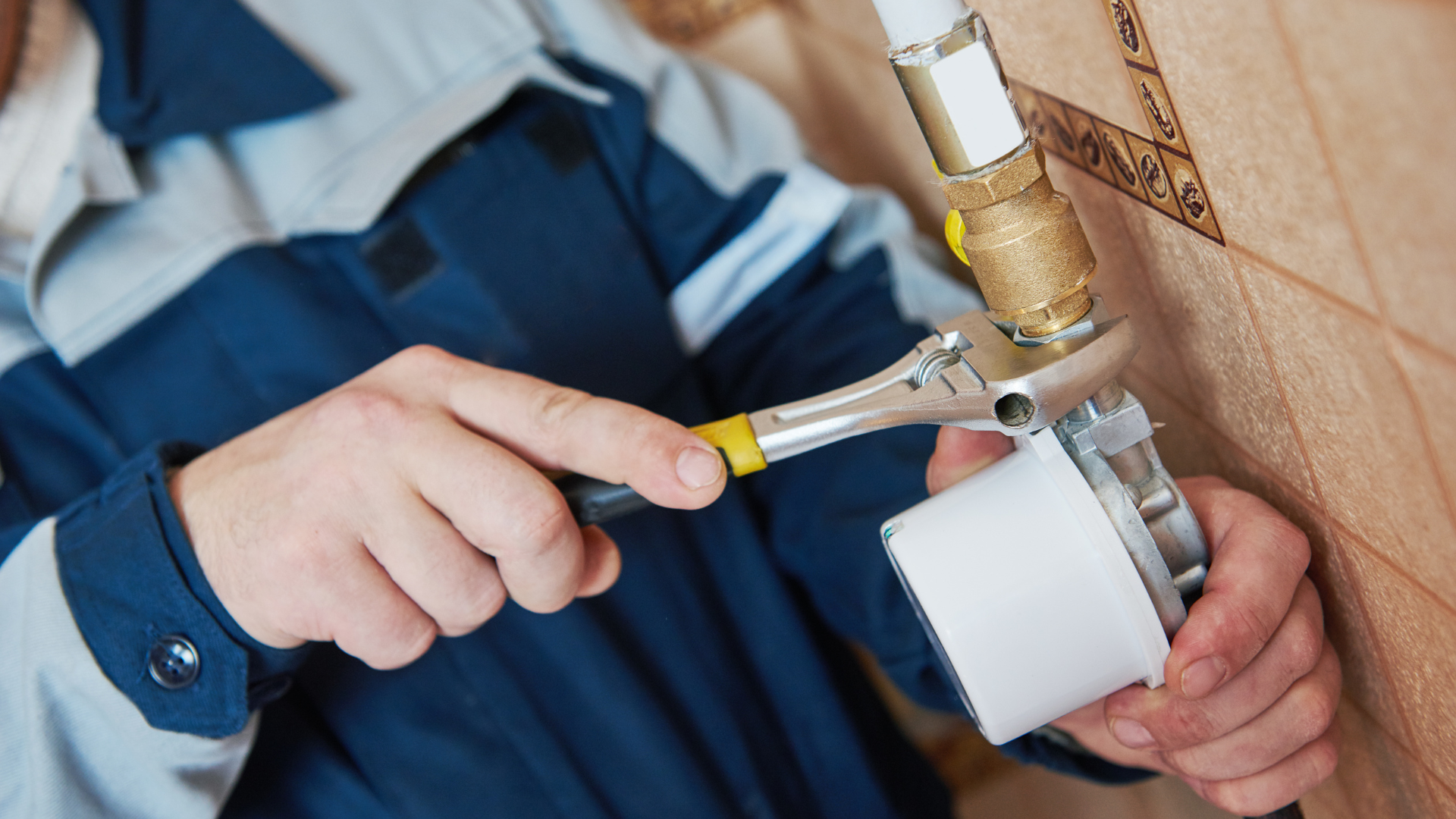 Plumber using a wrench to tighten a fitting on a pipe near a tiled wall.