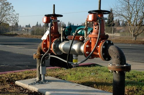 Two red water valves connected by pipes on a concrete base, outdoors.
