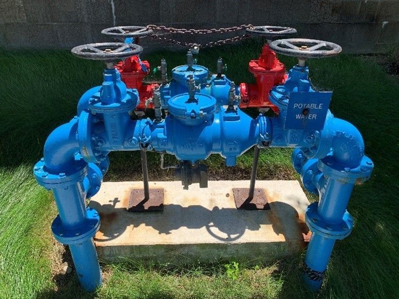 Blue and red water valves on a concrete base, set in a grassy outdoor area.
