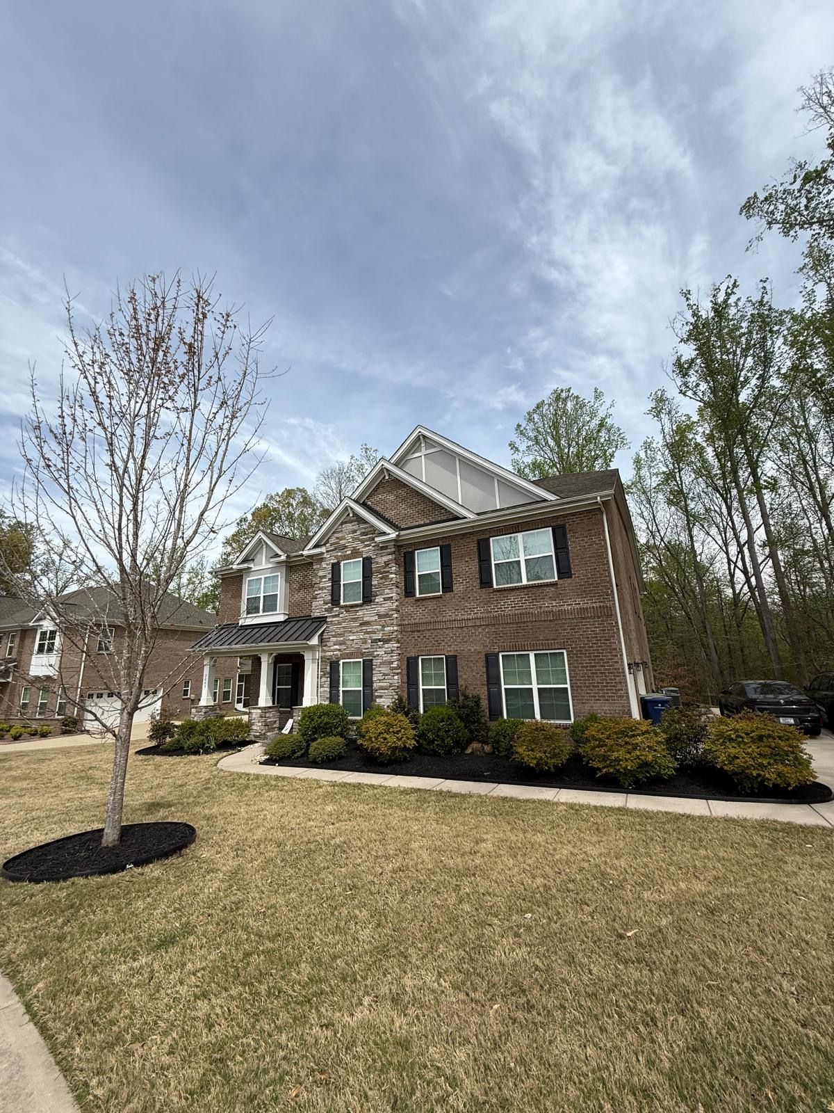 Two-story brick house with black shutters, landscaping, and a cloudy sky.