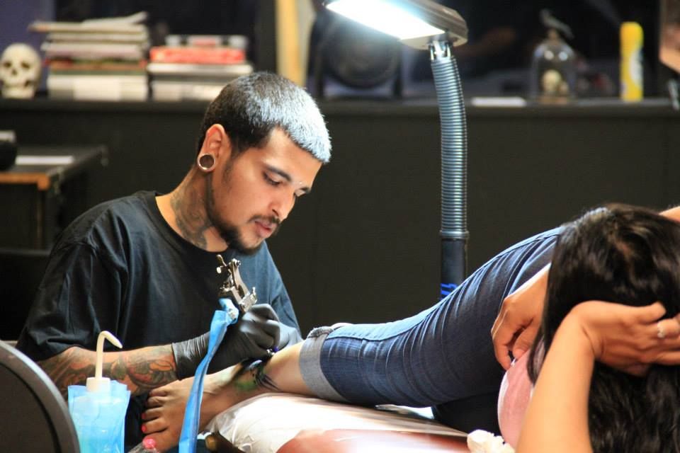 Tattoo artist with a black shirt and a customer; they're in a tattoo parlor with a lamp shining on the leg being tattooed.