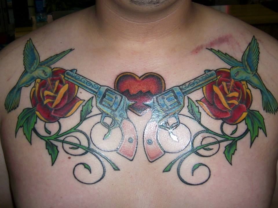 Tattoo on a chest of two revolvers, roses, hummingbirds, and a heart.