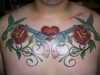 Tattoo on a chest of two revolvers, roses, hummingbirds, and a heart.