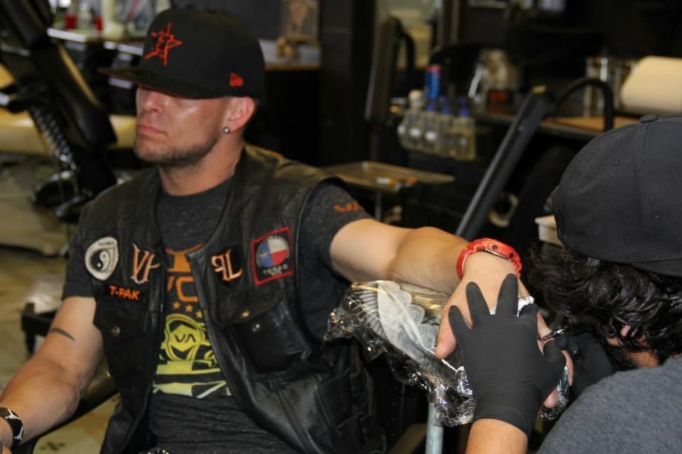 Man in leather vest gets tattoo on arm, in tattoo shop.
