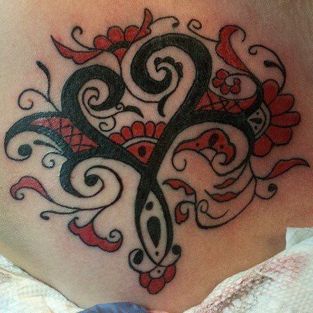 Black and red ornate tattoo with floral and swirl designs on skin.