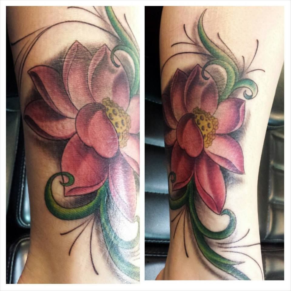 Pink and purple lotus flower tattoo with green vines on a forearm.