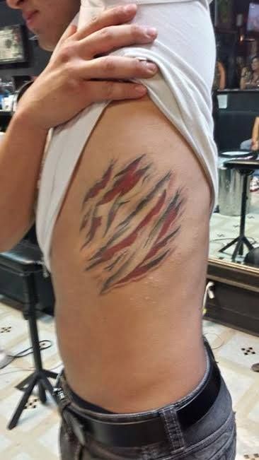 Tattoo of torn skin on a person's side, showing red and gray shading. Person in a white shirt and jeans.