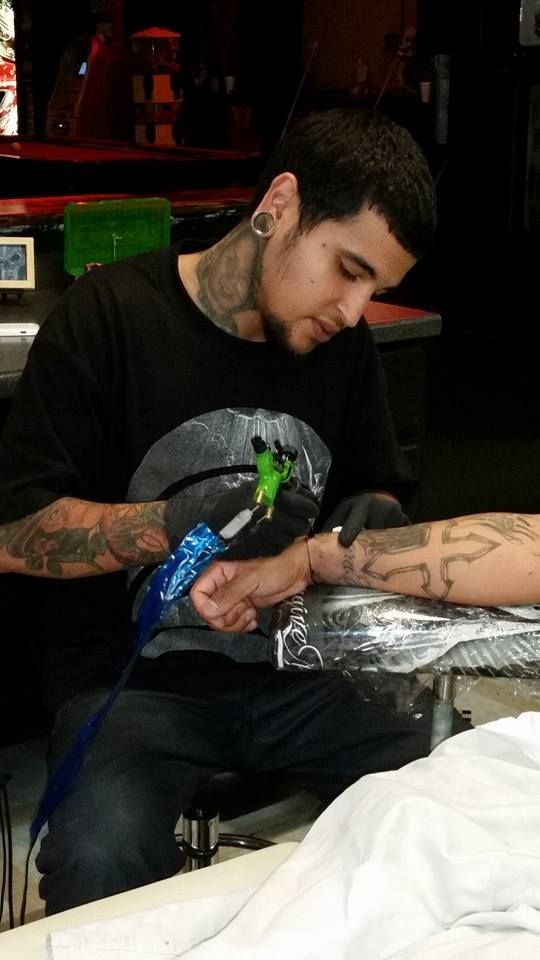 Tattoo artist in black shirt tattoos a forearm in a shop.
