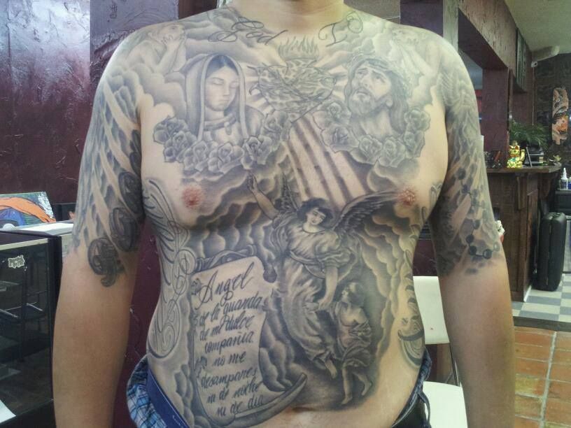 Man with large, gray chest and arm tattoos of angels, portraits, and script.