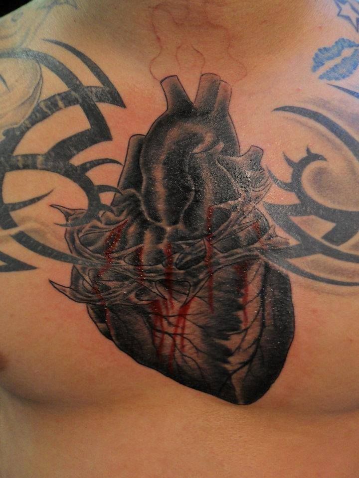 Black anatomical heart tattoo with thorns and red blood drips on chest.