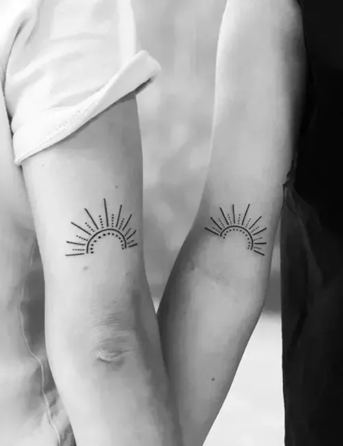 Two arms with matching sun tattoos on the inside of the forearms, in a grayscale photo.