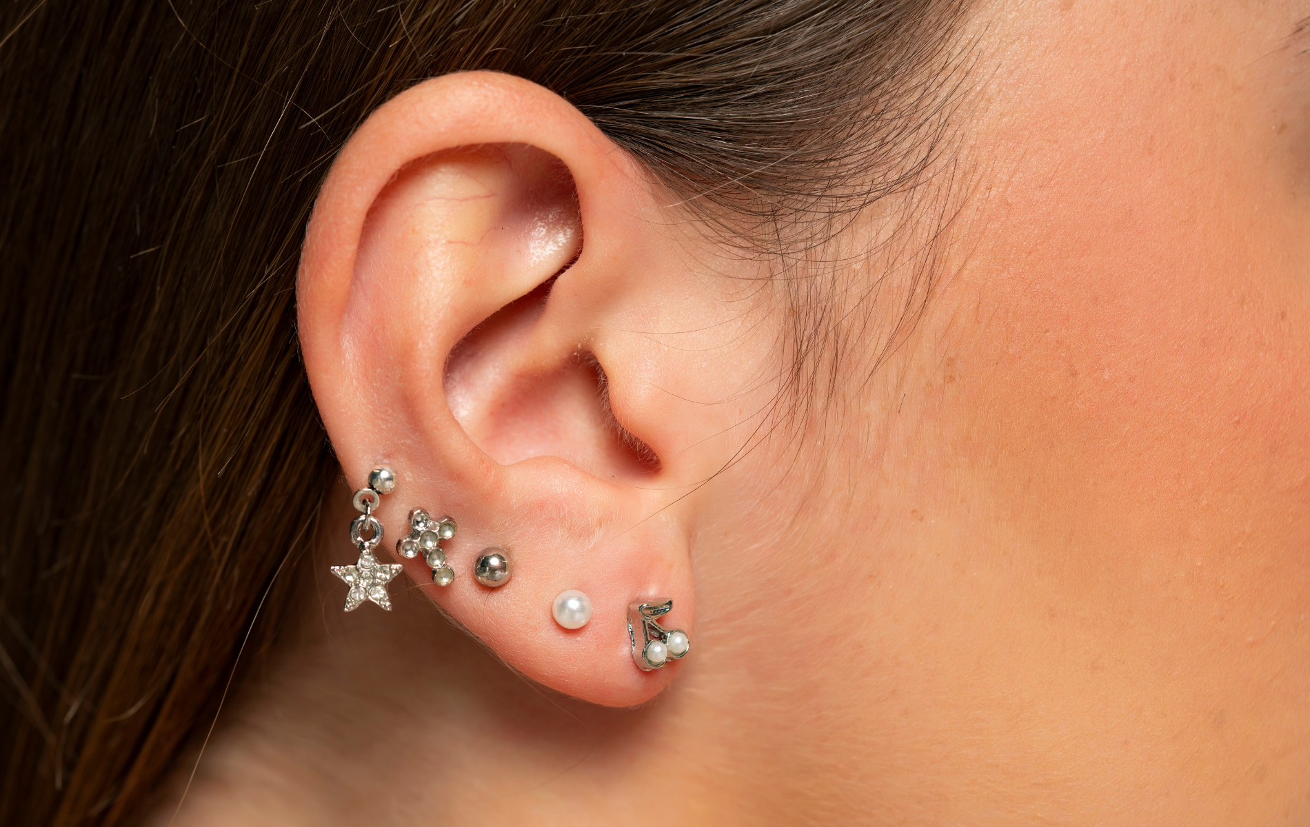 Ear with multiple silver earrings, including stars and studs.