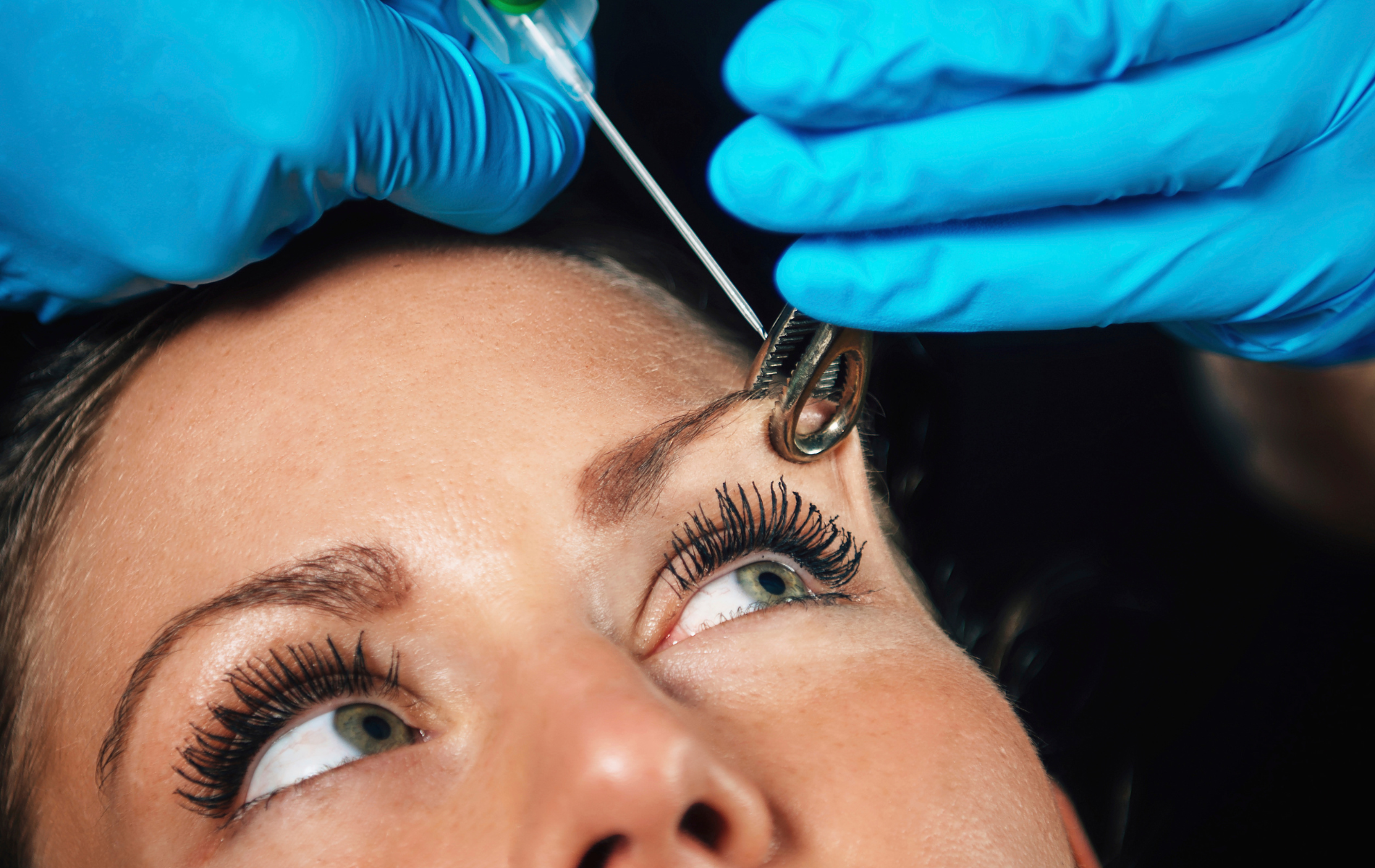 Person's eyebrow being pierced; gloved hands hold tools, close-up shot.