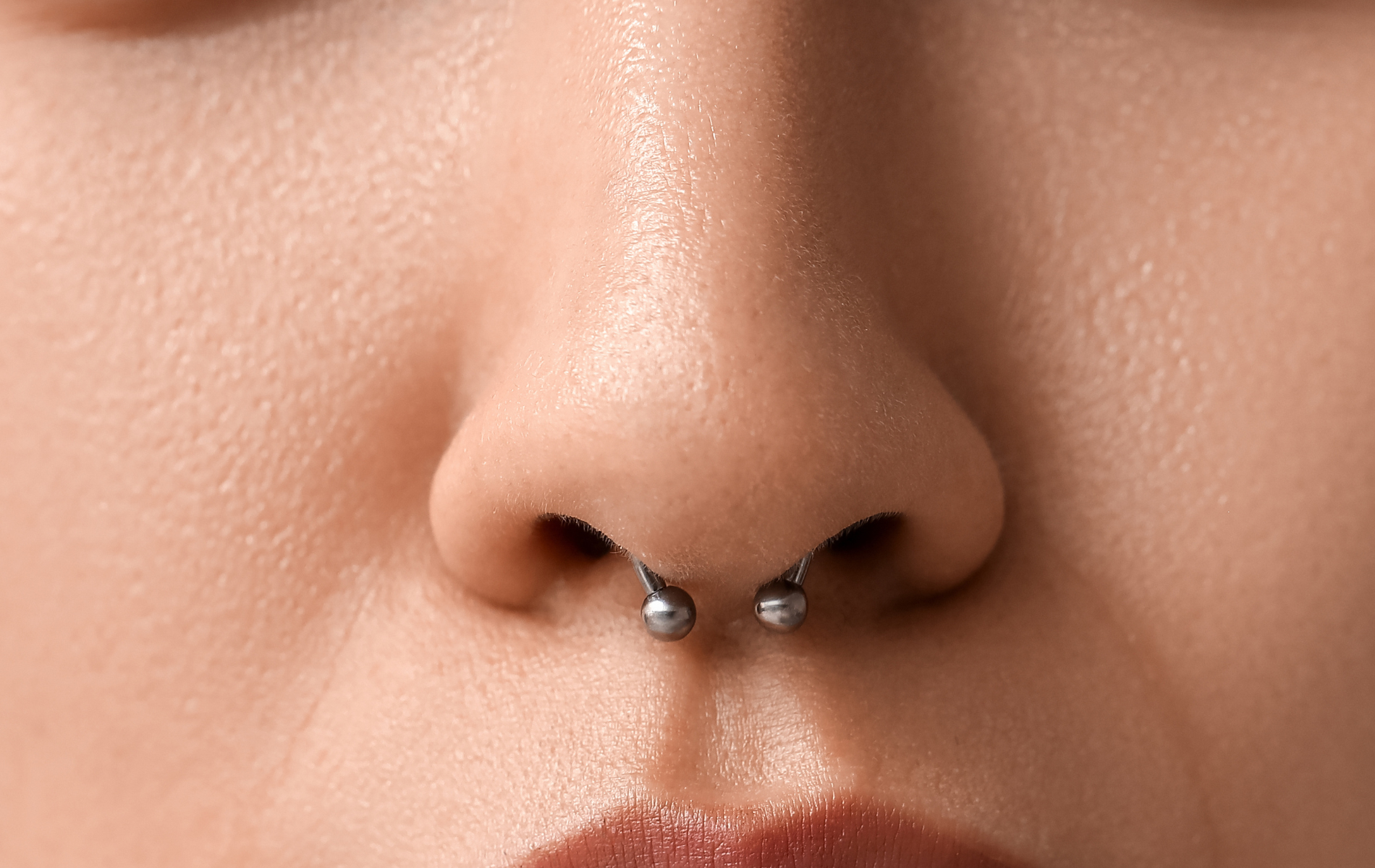 Close-up of a person's nose with a septum piercing. The piercing is a horseshoe-shaped barbell.