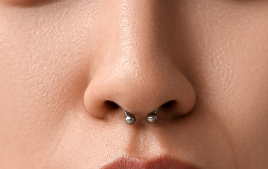 Close-up of a person's nose with a septum piercing. The piercing is a horseshoe-shaped barbell.