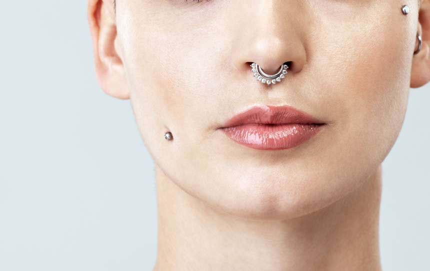 Close-up of a person's face with a septum and cheek piercings. Their skin is smooth.