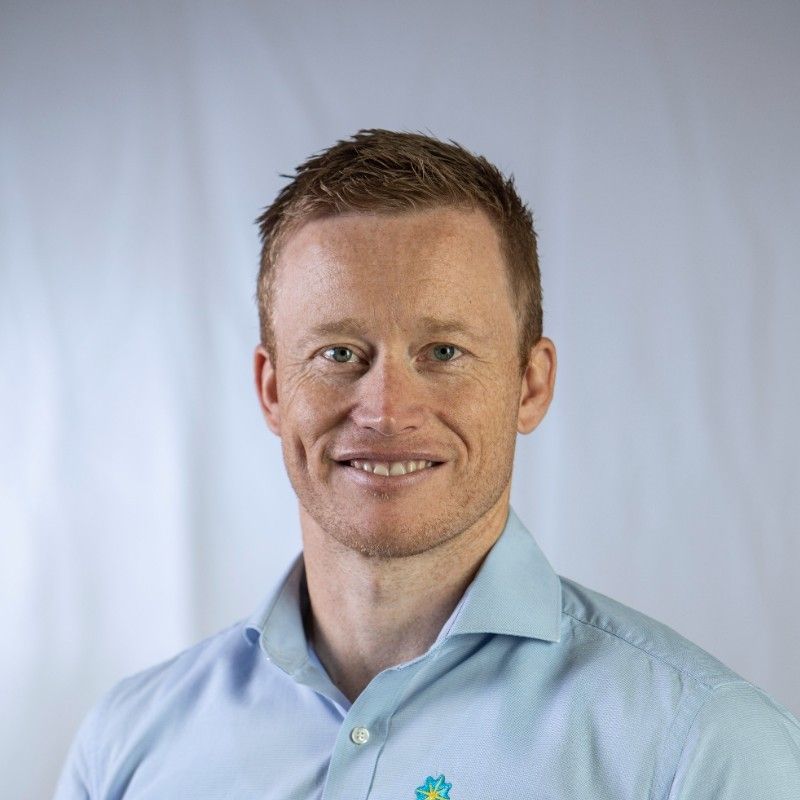 Man with red hair, smiling, wearing a light blue button-down shirt.