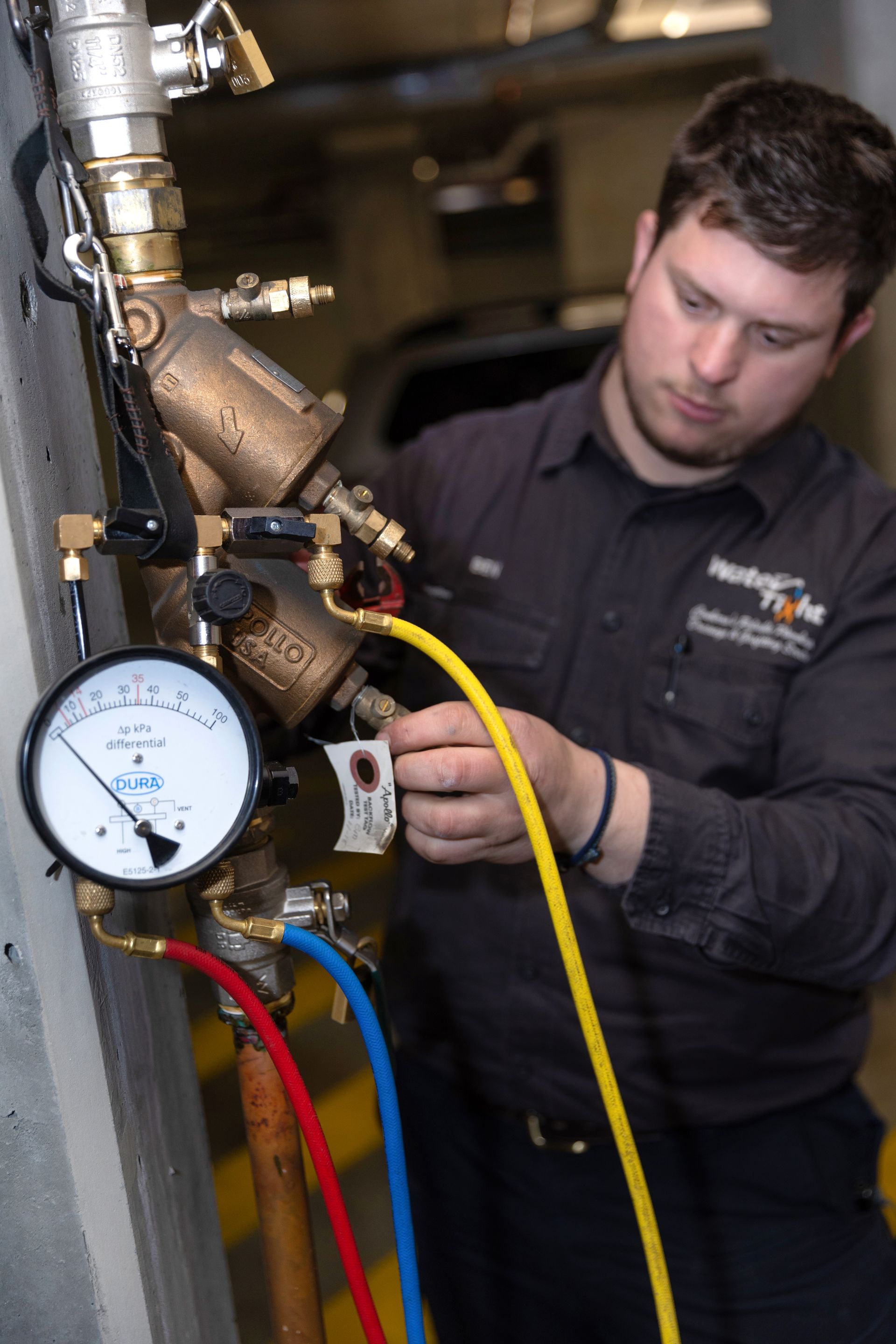 A man in a uniform inspects a gauge on an industrial machine, connecting a yellow hose.