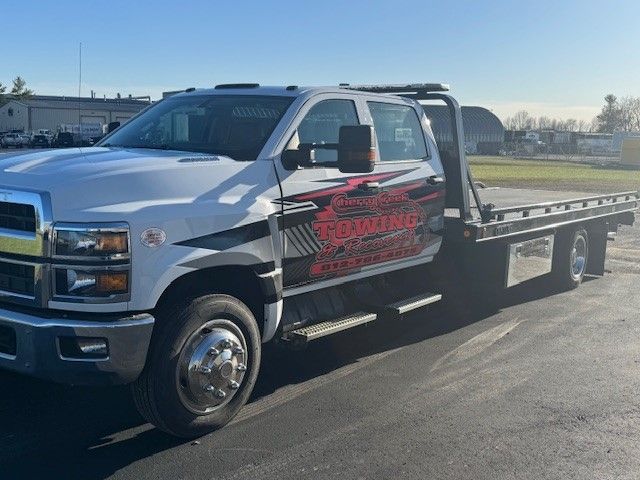 A white tow truck with a flat bed is parked in a parking lot.