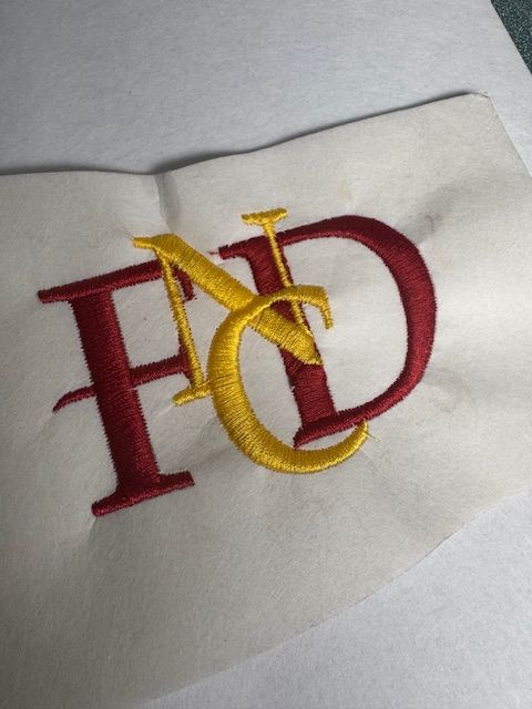 A red and yellow letter fd is embroidered on a piece of paper