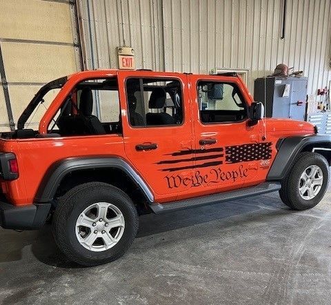A red jeep with the words `` we the people '' on the side is parked in a garage.