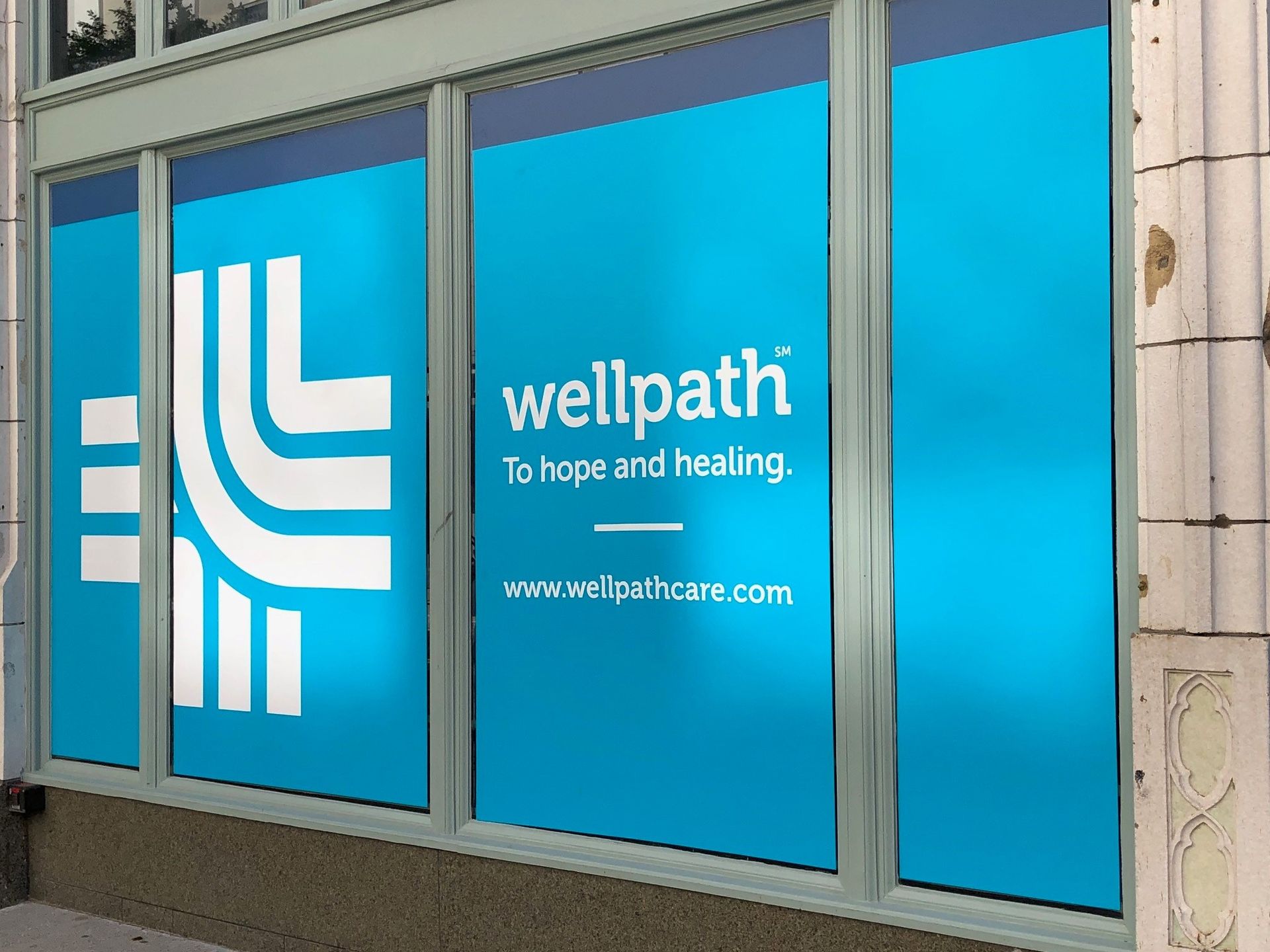 A blue sign on a window says wellpath to hope and healing