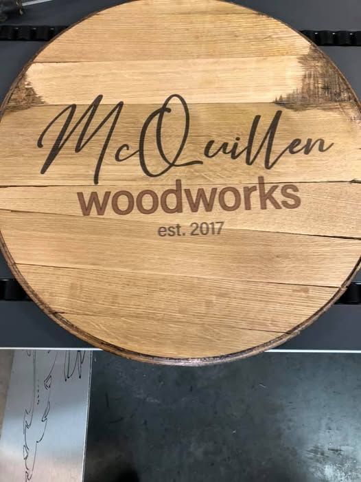 A wooden sign that says `` mcquillen woodworks '' is sitting on a table.