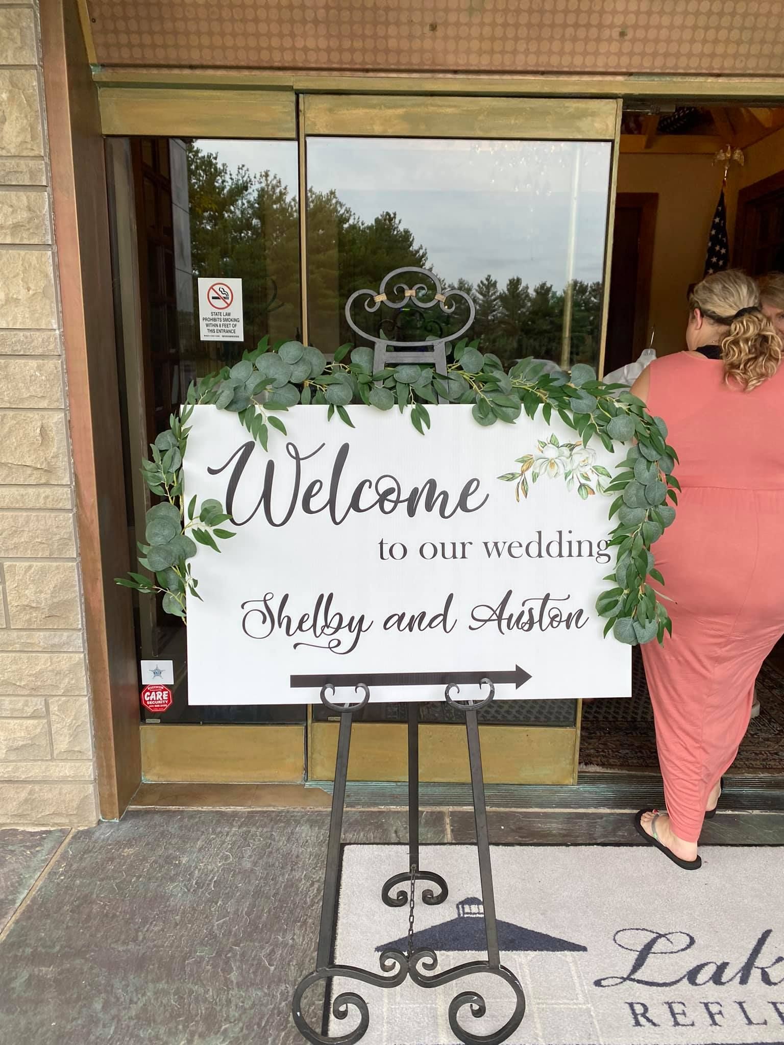 A woman is standing in front of a welcome sign for a wedding.