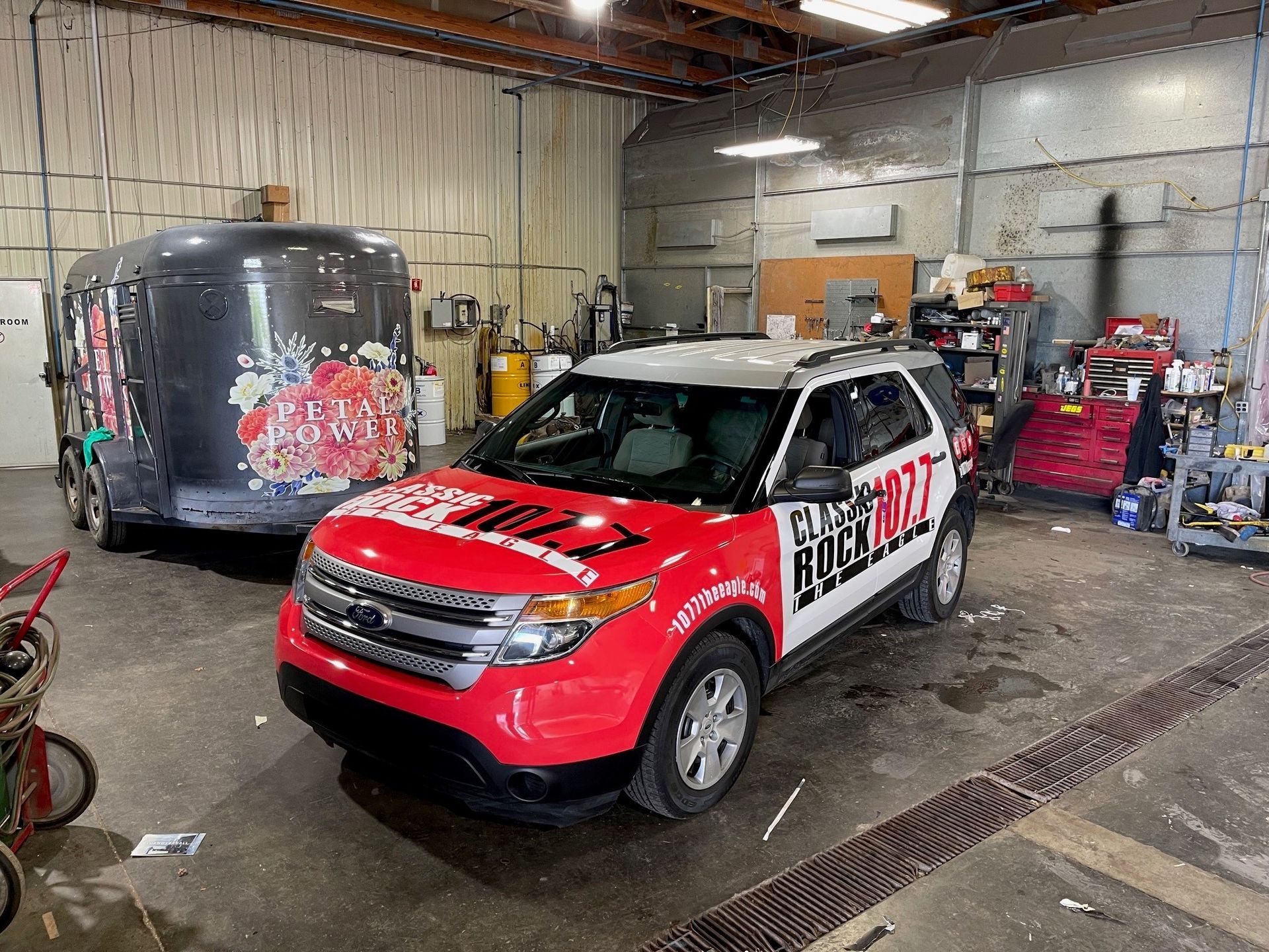 A red ford explorer is parked in a garage next to a trailer.