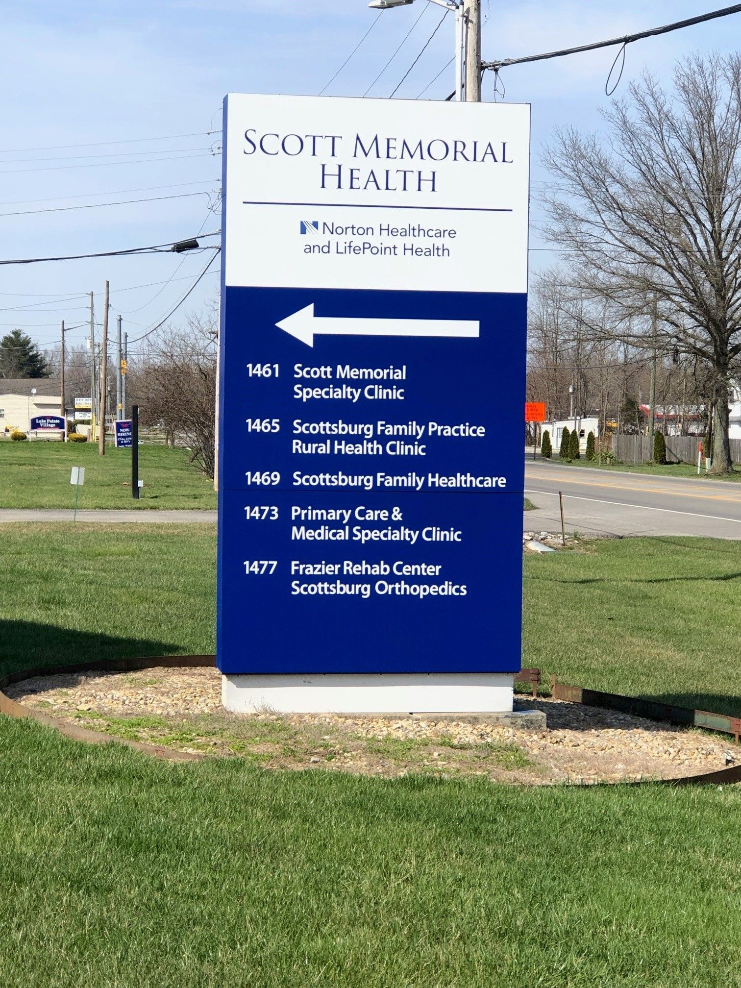 A blue and white sign for scott memorial health is sitting in the middle of a grassy field.