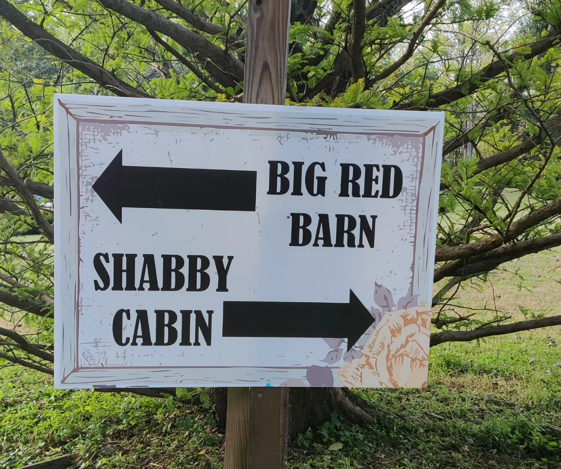 A sign points to shabby cabin and big red barn