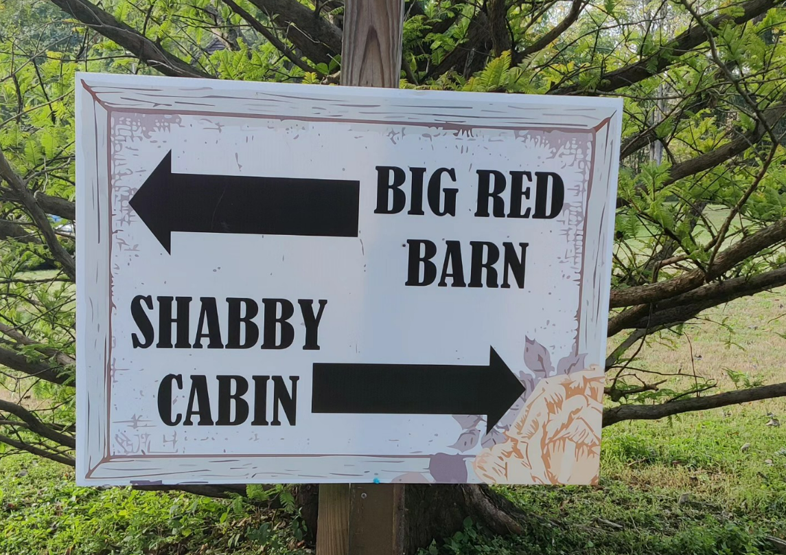 A sign pointing to big red barn and shabby cabin