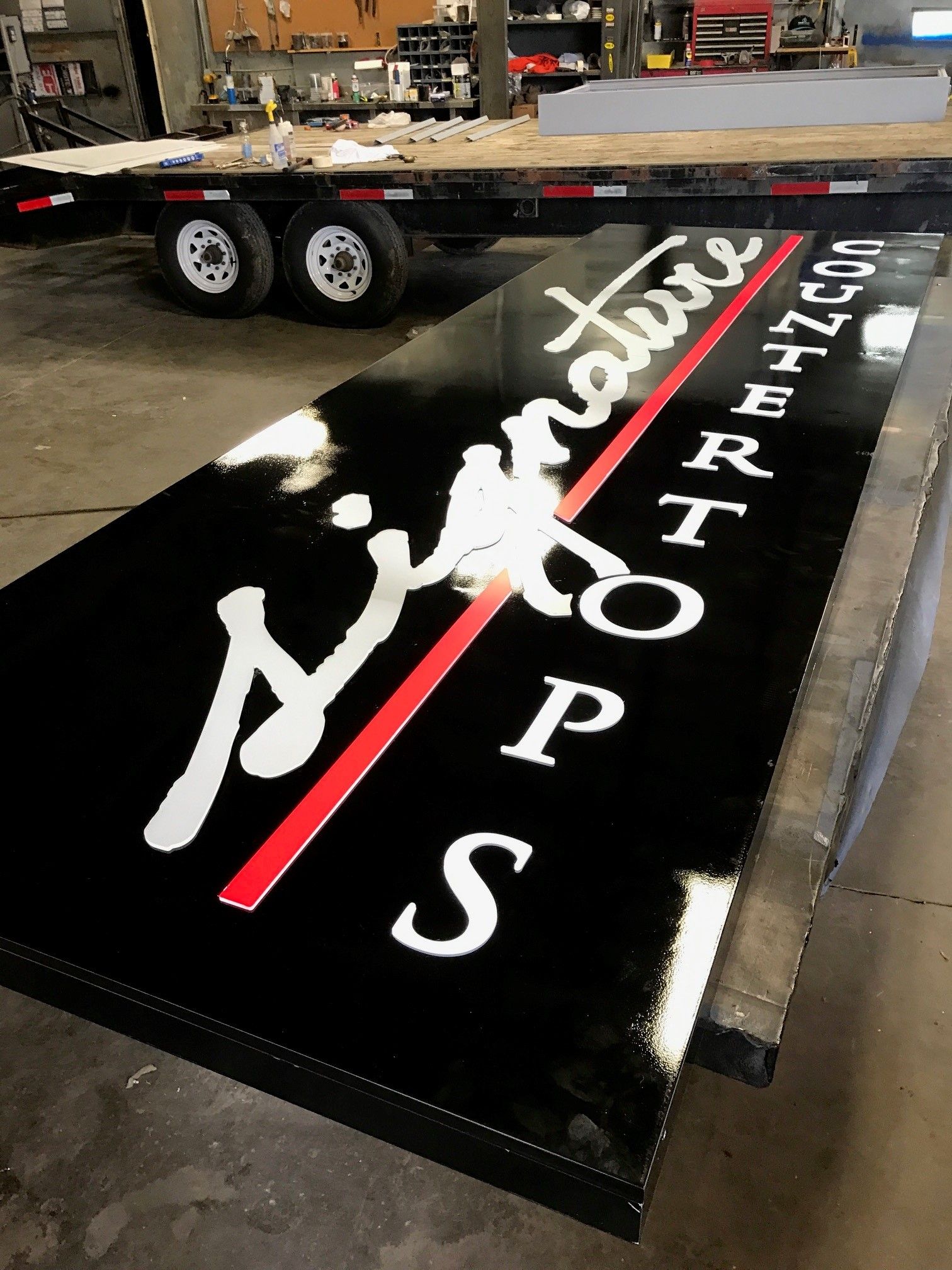 A large black sign with white letters on it is sitting on a table next to a trailer.