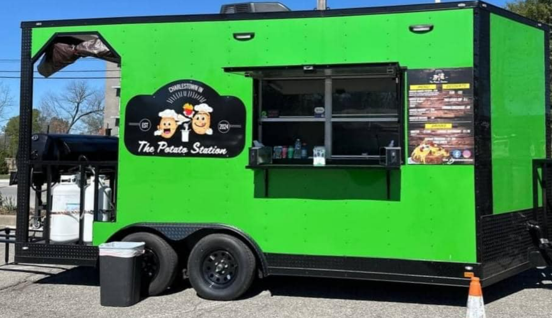 A green and black food truck is parked in a parking lot.