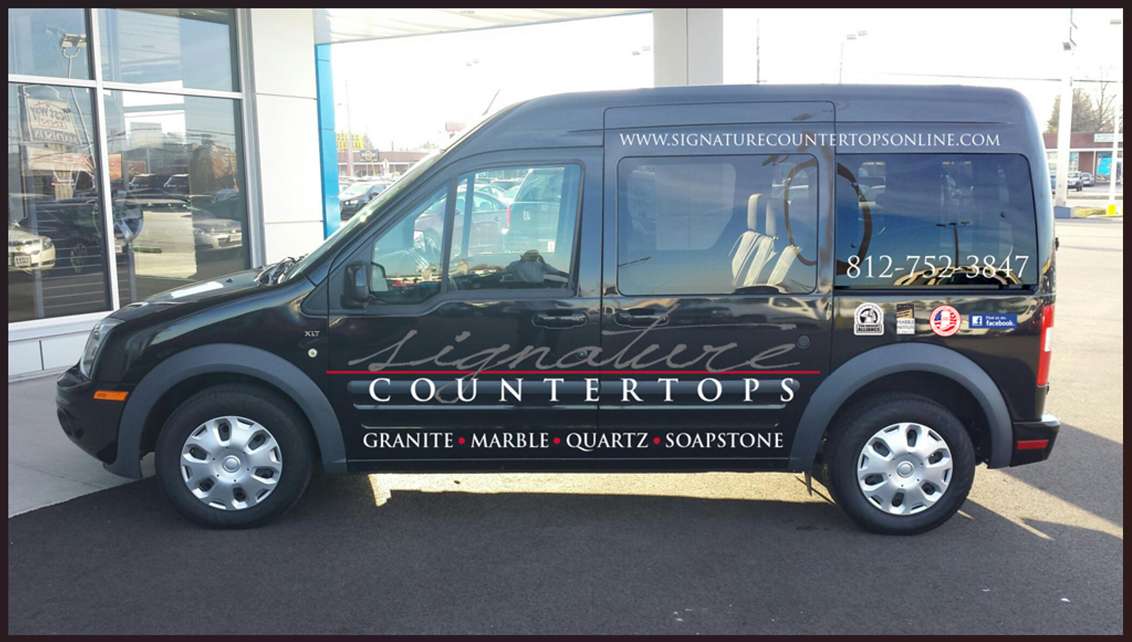 A black van with signature countertops written on the side is parked in front of a building.