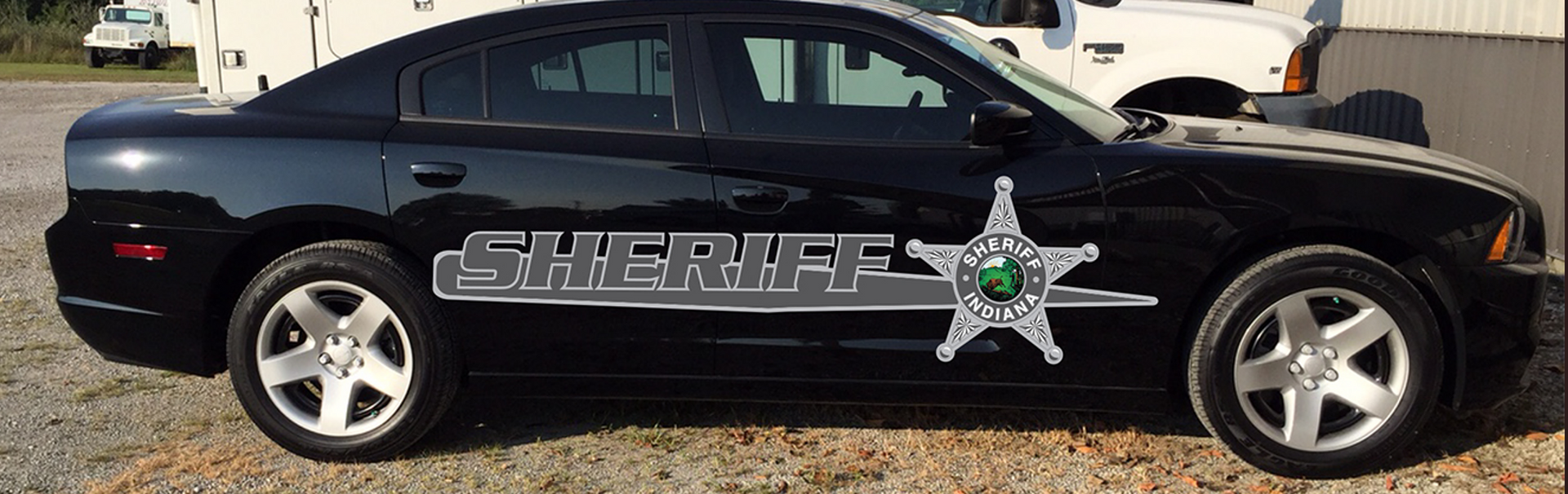A black sheriff 's car is parked in a gravel lot