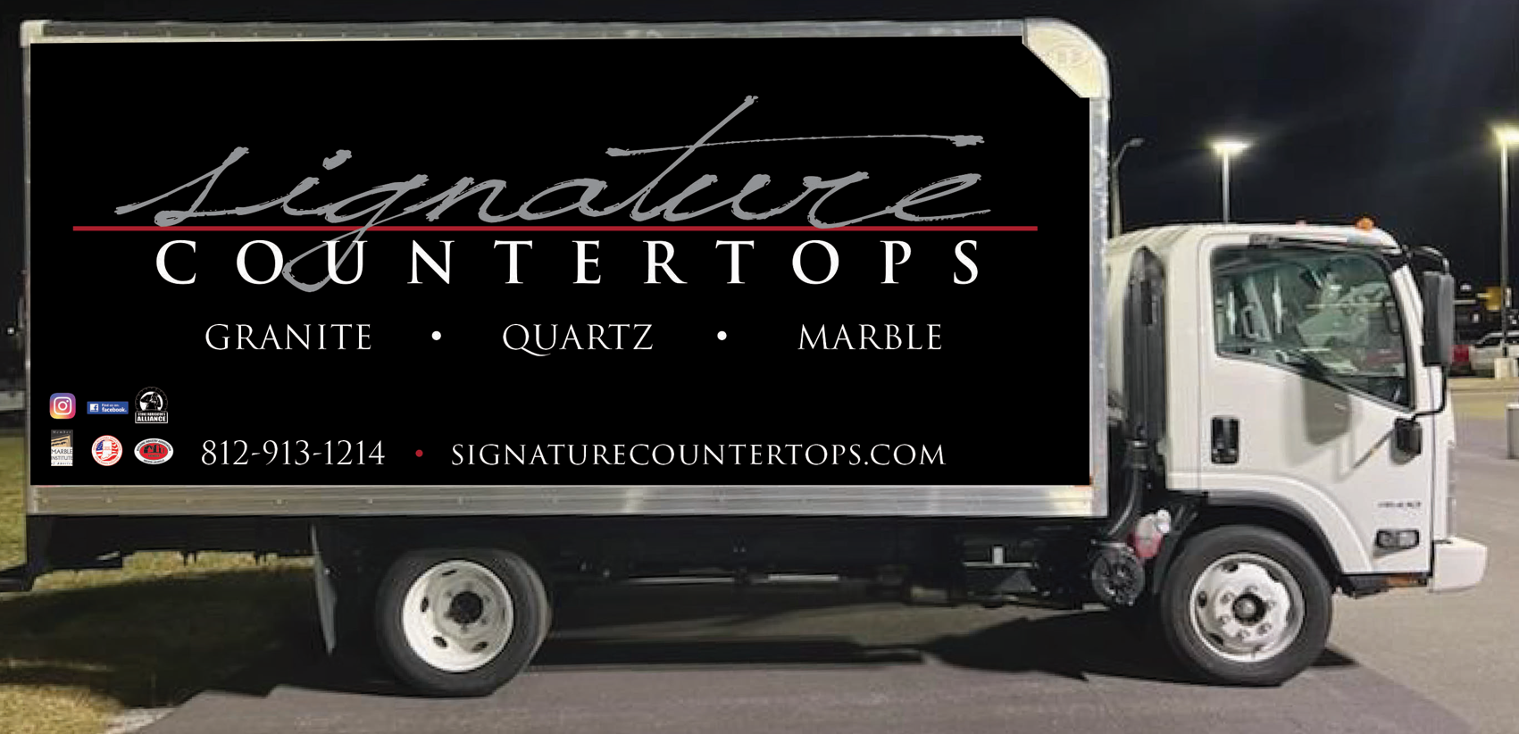 A signature countertops truck is parked in a parking lot at night.