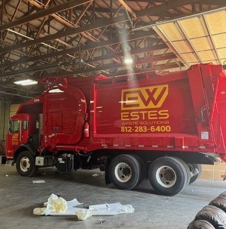 A red garbage truck is parked in a garage.
