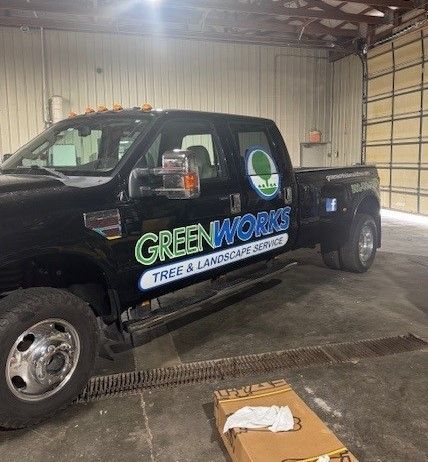 A black truck with the word greenworks on the side is parked in a garage.