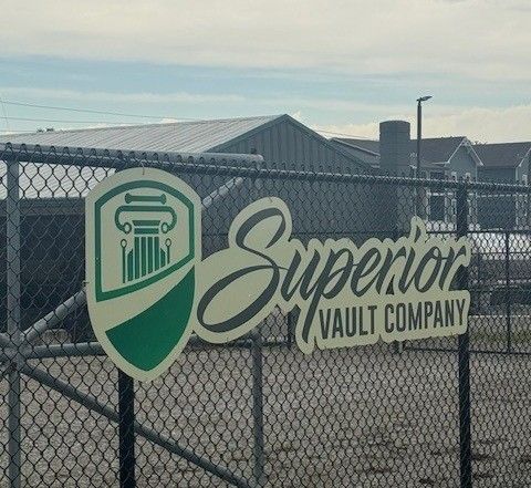 A sign on a chain link fence says superior vault company