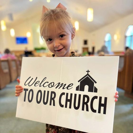 A little girl is holding a sign that says welcome to our church