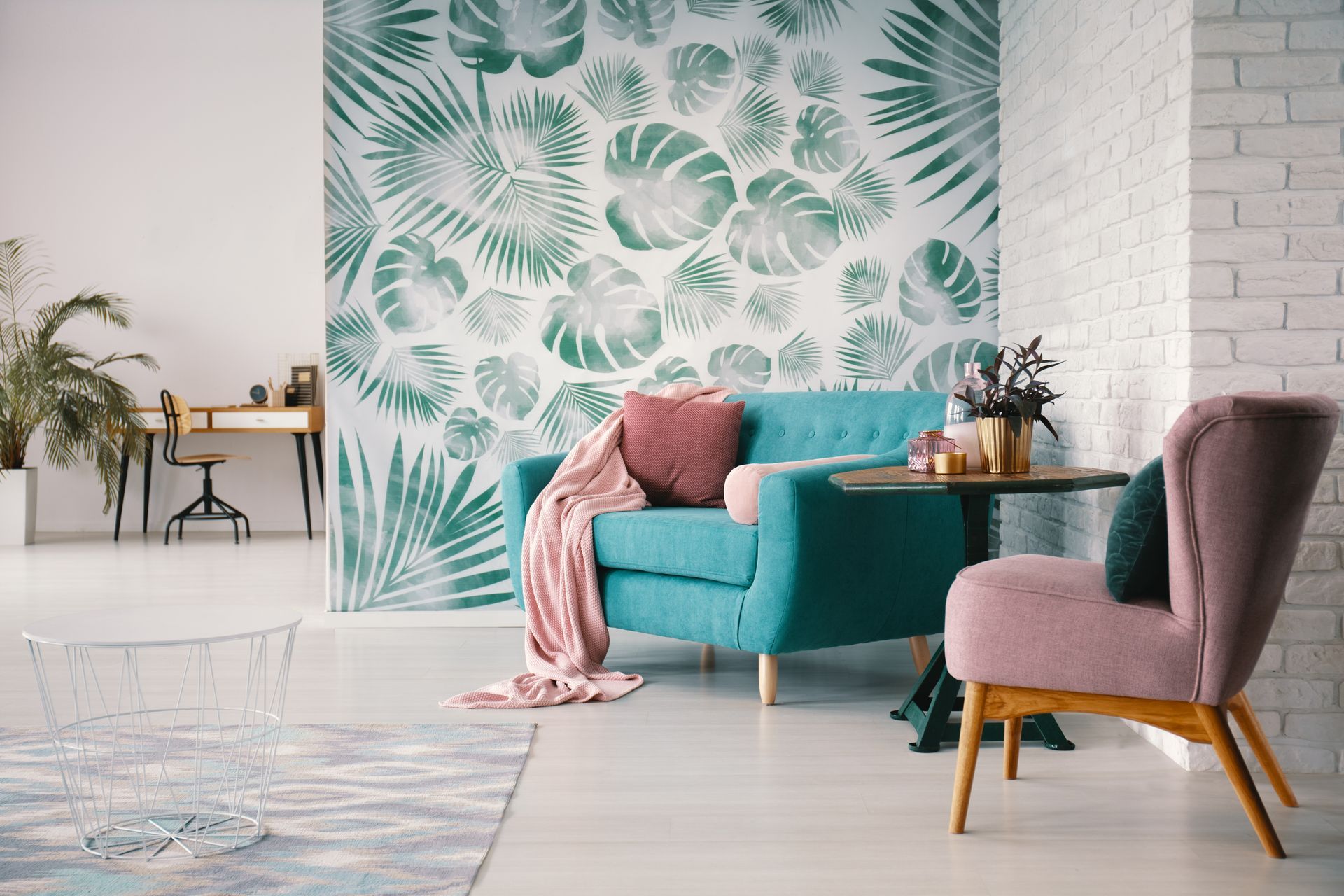 Living room with teal and pink furniture, tropical leaf wallpaper, and a brick wall.