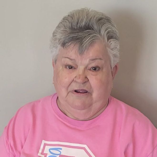 An older man is standing in a greenhouse holding a cell phone.