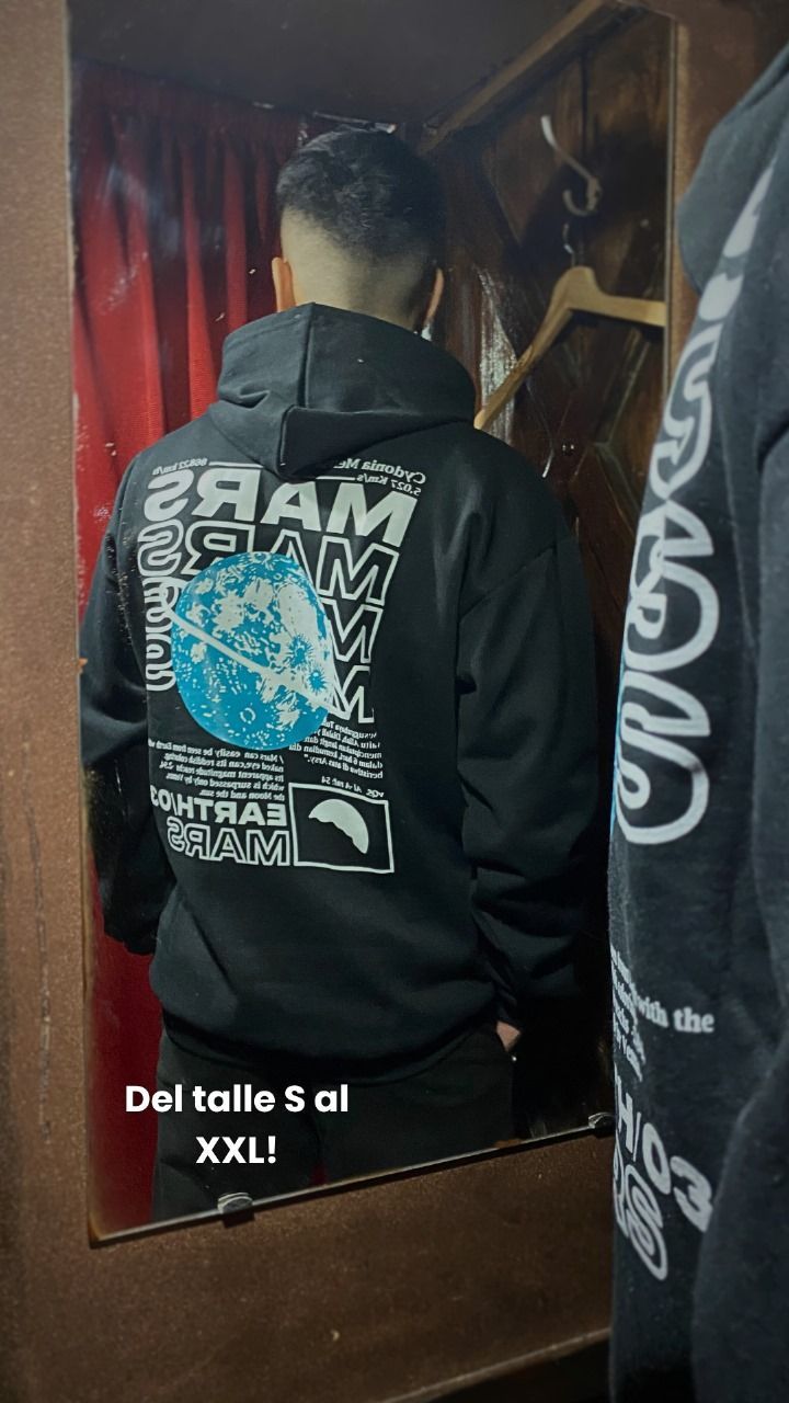 Hombre con sudadera negra con texto blanco, mano cerca de la cara, en el interior.