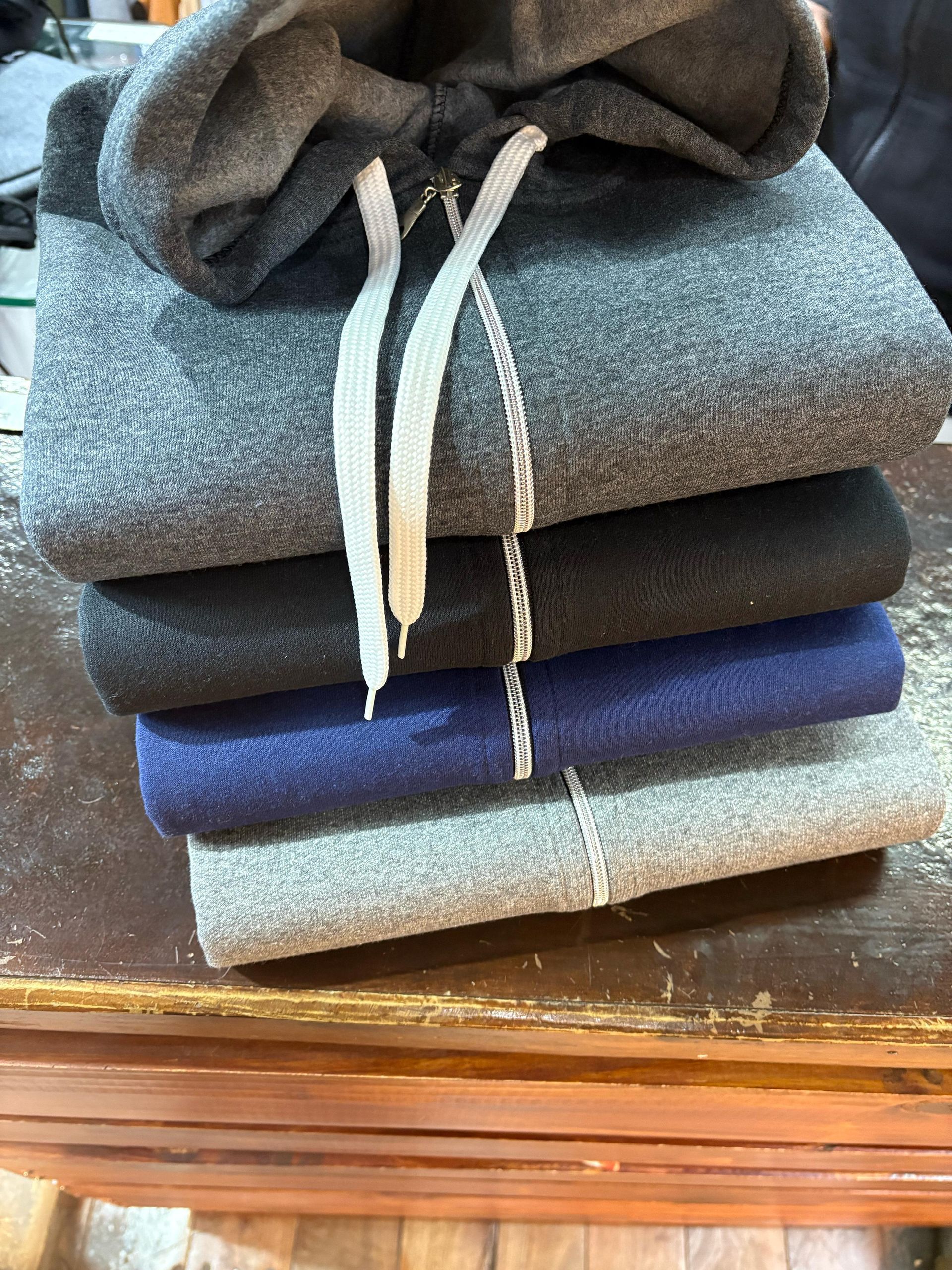 Hombre con sudadera gris y pantalones deportivos, de pie con las manos en los bolsillos, en una puerta.