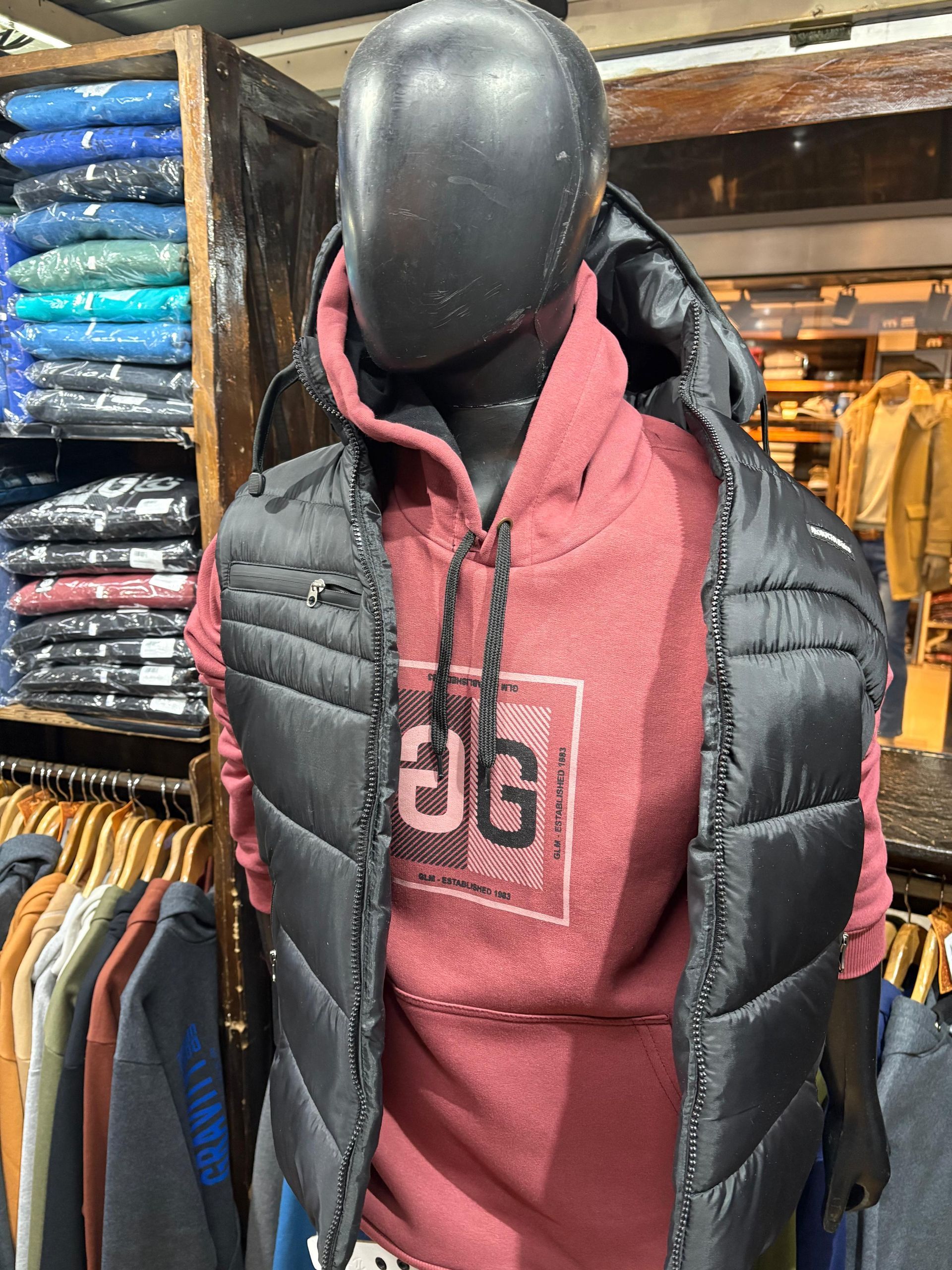 Maniquí que lleva un chaleco negro sobre una sudadera con capucha roja en una tienda de ropa.