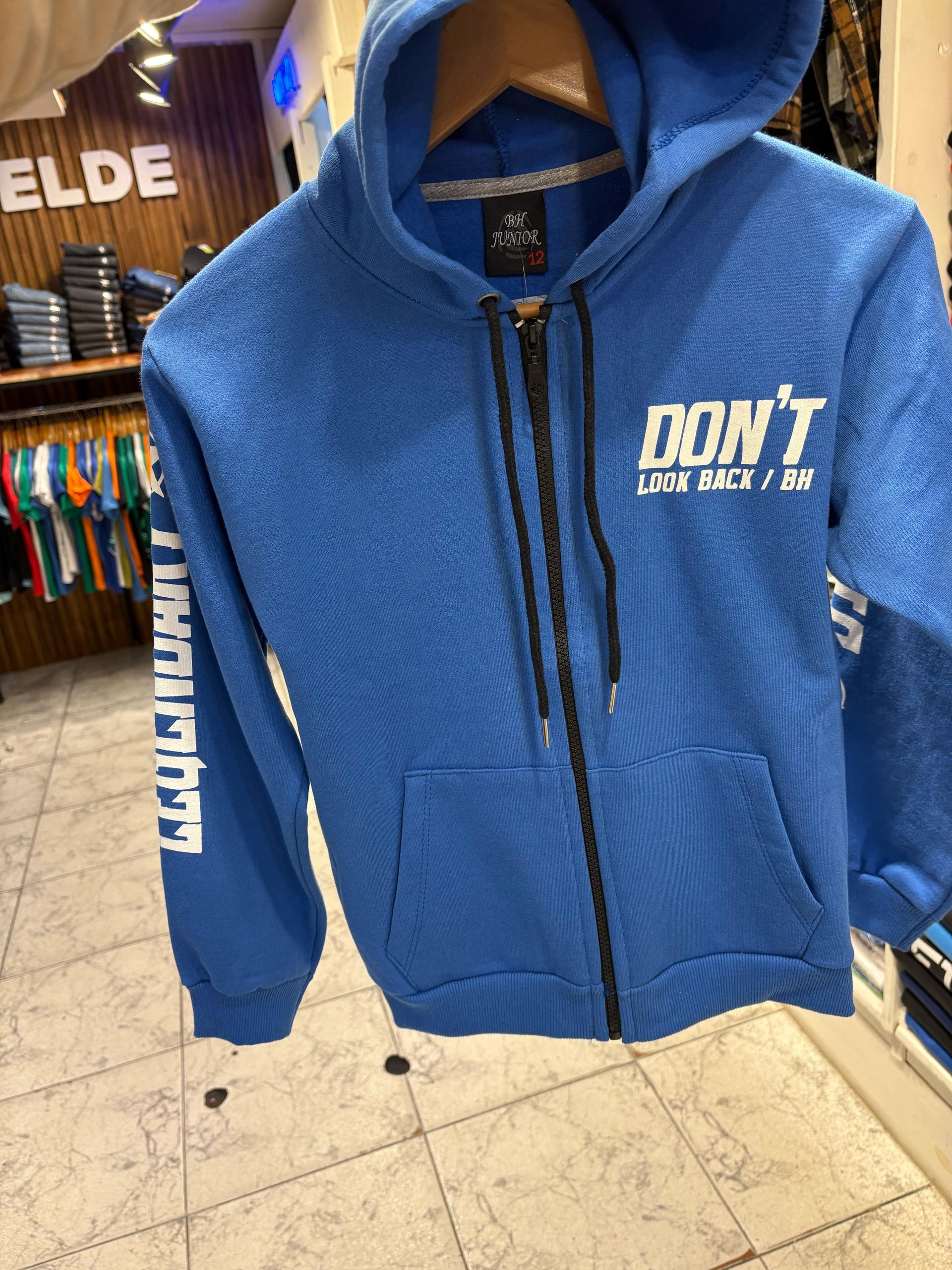 Niño con chándal negro y gorra, zapatillas blancas, en una tienda de telas, mirando hacia abajo.